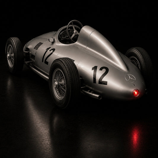 Silver Mercedes racing car number 12 viewed from the rear against a black background with a glowing red taillight.